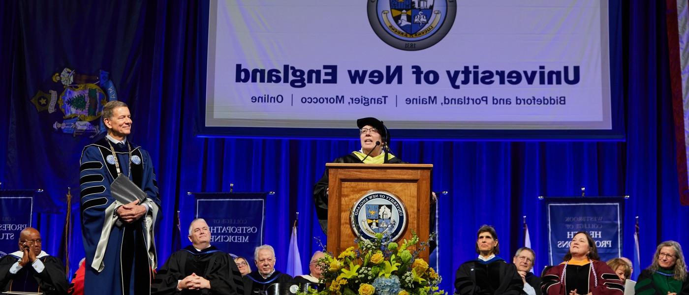在2023年的毕业典礼上，一名教员在讲台上发言，其他教员和大学校长在一旁观看